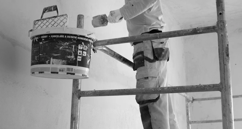 Maalaustyömaa, jossa maalari työskentelee turvallisesti telineillä asianmukaisissa suojavarusteissa.